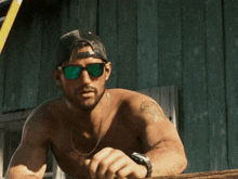 a shirtless man wearing sunglasses and a baseball cap stands in front of a wooden wall