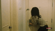 a woman in a plaid shirt is opening a door in a room with a full logo on the bottom right