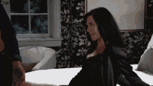 a woman in a black robe is sitting on a bed with a man holding her hand