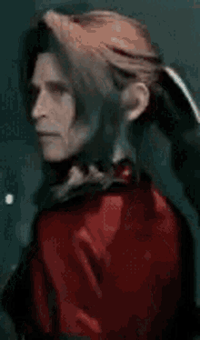 a woman with long hair and a red jacket is standing in front of a window and looking at the camera .