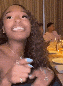 a woman is smiling while sitting at a table with plates and silverware .