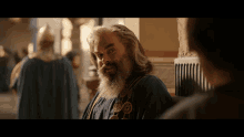 a man with a beard and a blue robe stands in front of a wall