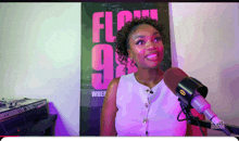 a woman stands in front of a microphone in front of a poster that says flow 98