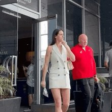 a man in a red shirt stands next to a woman in a white dress in front of a building that says cocktails