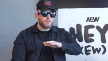 a man wearing sunglasses stands in front of a sign that says aew