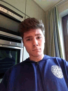 a man wearing a blue sweatshirt that says ' r.l.c. ' on it stands in front of an oven