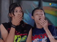 two girls are covering their mouths with their hands and one has a shirt that says ' opeye ' on it