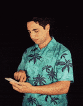 a man in a blue shirt with palm trees on it is looking at his phone