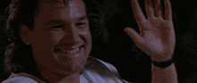 a man with curly hair is smiling with his arms outstretched in a dark room .