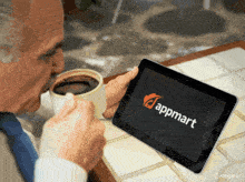 a man drinking coffee while looking at a tablet that says appmart on it
