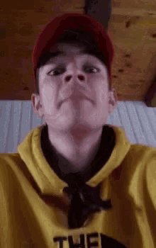a young man is wearing a yellow hoodie and a red hat .