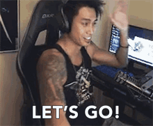 a man wearing headphones is sitting at a desk with a computer and says let 's go .