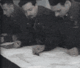 a group of men are looking at a piece of paper and one of them has a ring on his finger