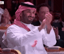a man in a keffiyeh sits in a chair clapping