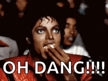 a man in a red jacket is eating popcorn while watching a movie and says `` oh dang !!! '' .
