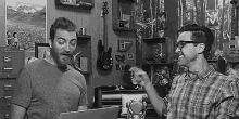 two men are standing next to each other in a room talking to each other .