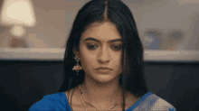 a woman wearing a blue saree and gold earrings looks serious