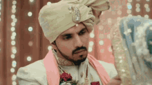the groom is wearing a turban and looking at the bride 's wedding dress .
