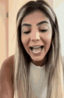 a woman with blonde hair and brown eyebrows is laughing with her mouth open
