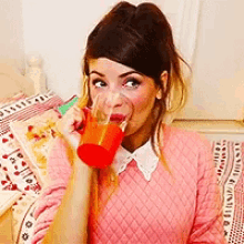 a woman wearing a pink sweater is drinking from a red cup