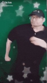 a man in a black shirt and hat is standing in front of a green wall .