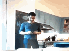 a man in a blue shirt is standing in a kitchen looking at his cell phone