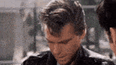 a man in a leather jacket is looking down at something while another man looks on .