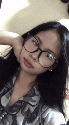 a woman wearing glasses takes a selfie with her hand on her chin