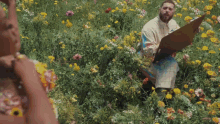 a man is sitting in a field of flowers holding a drawing board