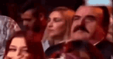 a man with a mustache is sitting in the audience at a concert .