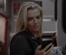 a woman in a black vest with the letter u on it looks at her phone