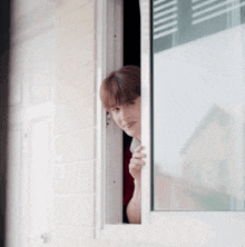 a woman is peeking out of a window while holding a cup