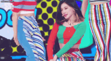 a woman in a crop top and striped pants is dancing on a stage with other women .