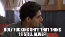 a man is sitting at a table with the words `` holy fucking shit ! that thing is still alive ? '' .