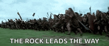 a large group of soldiers are running in a field with the words `` the rock leads the way '' written above them .