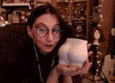 a woman wearing glasses is holding a cup that looks like a buttocks