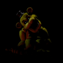 a yellow teddy bear with a top hat is in the dark .