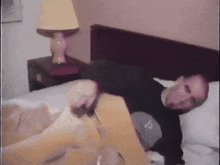 a man in a black shirt is laying on a bed with a lamp in the background