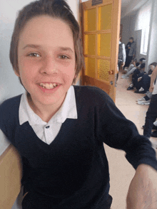 a young boy in a black sweater smiles in front of a yellow door that says ' a ' on it