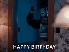 a man in a clown mask is standing in a doorway in a dark room and says `` happy birthday '' .