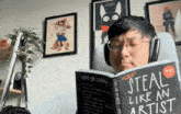 a man wearing headphones is reading a book titled " steal like an artist "