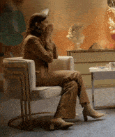 a woman in a brown suit sits in a chair with her hands over her mouth