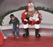 a little girl is crying while sitting on santa 's lap while a boy looks on