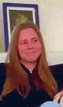 a woman with long red hair is sitting on a couch in front of a picture .