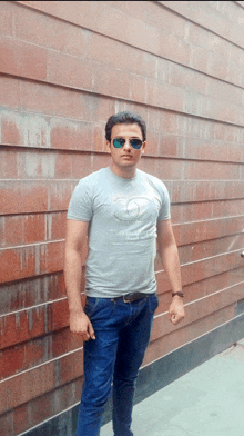 a man wearing sunglasses and a t-shirt with a heart on it stands in front of a wall