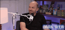 a man in a black shirt is sitting in front of a microphone with dark web written on the bottom