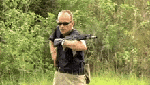 a man in sunglasses is holding a gun in a field .