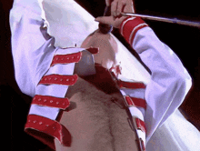 a man in a white shirt with red straps on the sleeves is holding a microphone