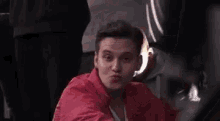 a man in a red jacket is smiling and looking at the camera while sitting in a chair .