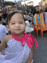 a little girl wearing a white polka dot dress and a pink ribbon around her neck